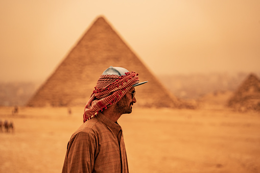 Giza, Cairo, Egypt - April 9, 2023 Bedouin man dressed in traditional clothes, in front of the Giza Necropolis pyramids complex. Egypt, Africa