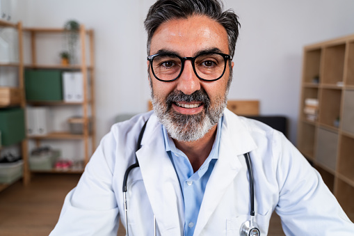 Confident male doctor with glasses smiling at the camera in a medical office setting