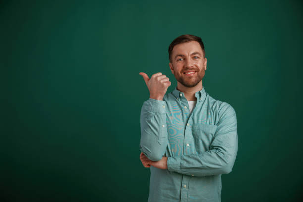 istock Showing to the side by finger to the empty space for text. Man is standing against background in the studio 2147701433