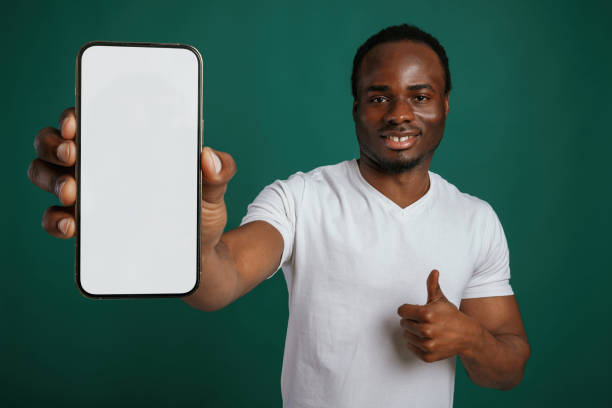 istock Smartphone with white empty space for text. African American man is standing against green background in the studio 2147701470