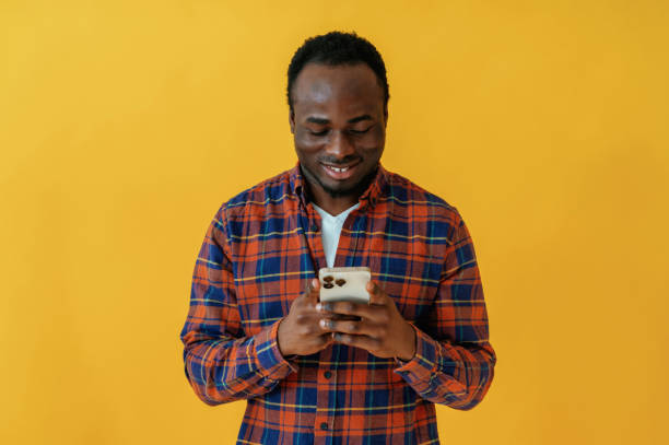 istock Smiling and holding smartphone. Black man is in the studio against yellow background 2147703250