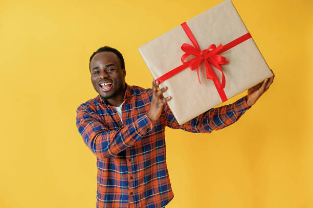 istock With big present gift box. Black man is in the studio against yellow background 2147703289