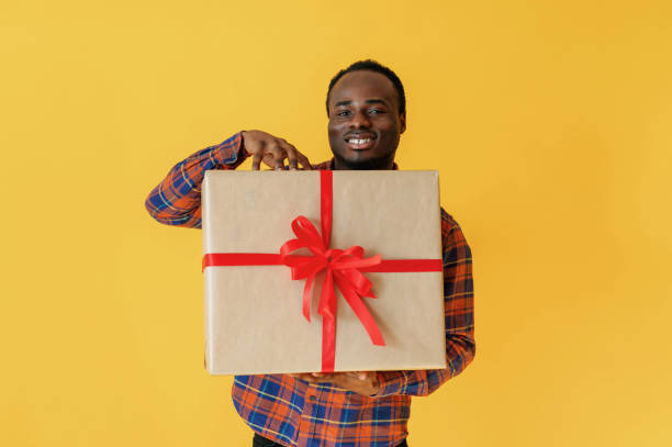 istock With big present gift box. Black man is in the studio against yellow background 2147703296