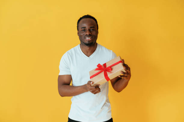 istock Holidays gift box in hand. Black man is in the studio against yellow background 2147703317