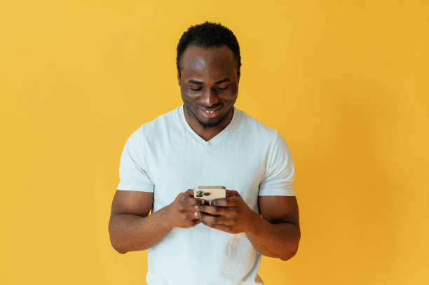 istock Holding smartphone and smiling. Black man is in the studio against yellow background 2147703324
