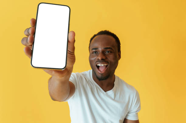 istock Empty display of smartphone, holding. Black man is in the studio against yellow background 2147703370