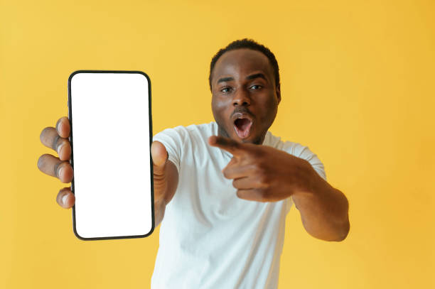 istock Empty display of smartphone, holding. Black man is in the studio against yellow background 2147703381