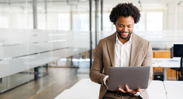 A young confident businesswoman in an ivory suit indoors A business professional works intently on a laptop, exuding focus and dedication in an office setting. Concept of business analytics, focused work ethic, and digital business management. black man laptop stock pictures, royalty-free photos & images