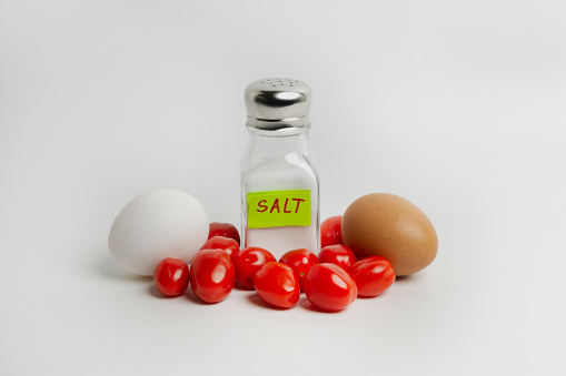 Eggs, tomatoes and salt in a salt shaker on a white background. Over-salting food is harmful to health. You need to salt your food in moderation.