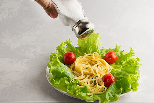 Pasta with vegetables is seasoned with salt on a gray background. Too much salt in food is unhealthy. It is necessary to salt food in moderation.