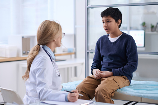 Portrait of young boy talking to doctor in clinic and explaining symptoms during check up examination