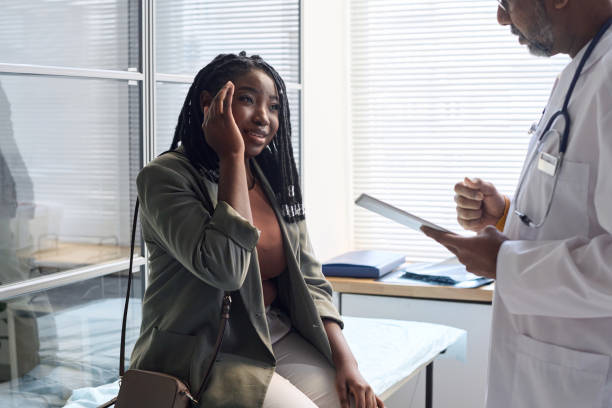 Black Woman Suffering From Headache in Clinic Portrait of African American woman suffering from headache explaining symptoms to doctor during consultation in clinic copy space doctor head stock pictures, royalty-free photos & images