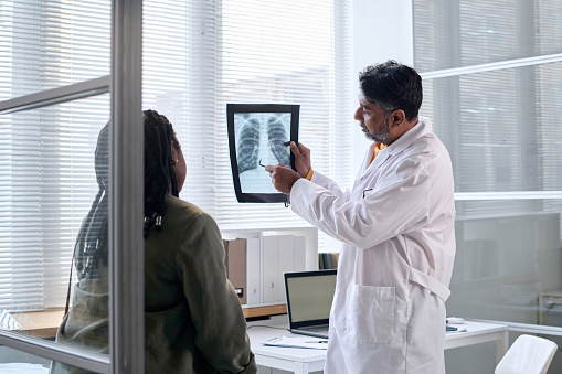 Side view portrait of senior doctor pointing at chest x ray while consulting patient in clinic copy space