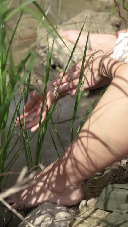 Detailed shot of a woman's hands scooping water from the river to refresh her arms among the streamside plants.