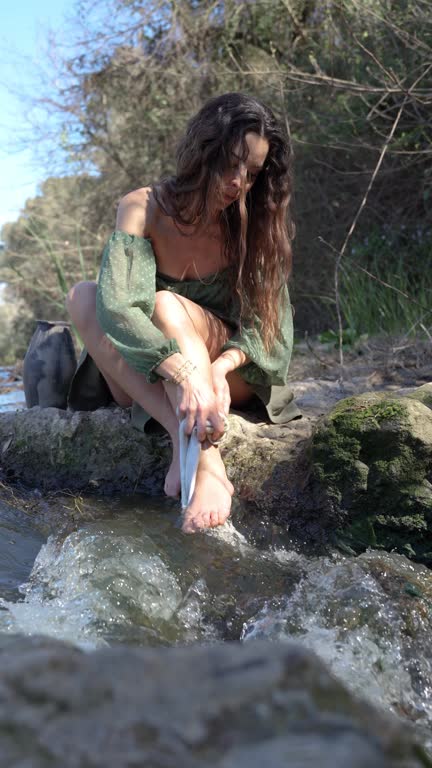 Woman washes her legs with water and soap while seated in the river.