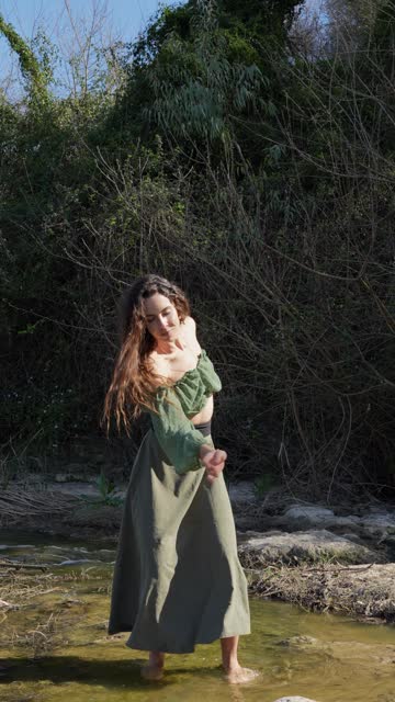 Young woman with closed eyes performs a rhythmic and natural dance with bare feet in the water in nature.