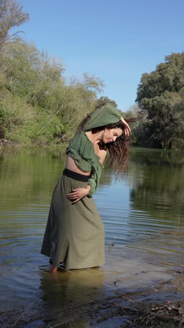 Woman joyfully dancing in the river water surrounded by lush greenery.