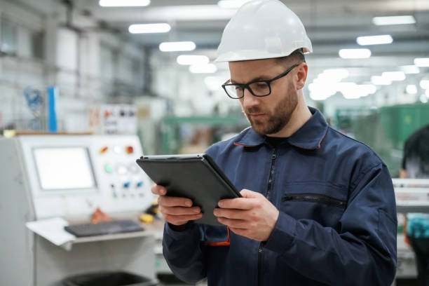 istock Looking and holding tablet. Factory worker is indoors with hard hat 2147708696