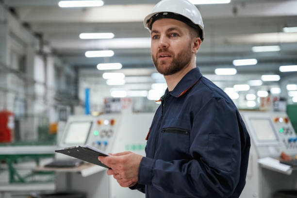 istock Looking far away, holding notepad. Factory worker is indoors with hard hat 2147709162