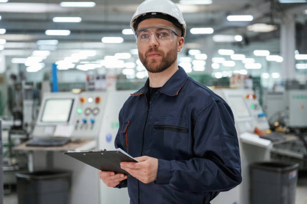 istock Looking far away, holding notepad. Factory worker is indoors with hard hat 2147709163