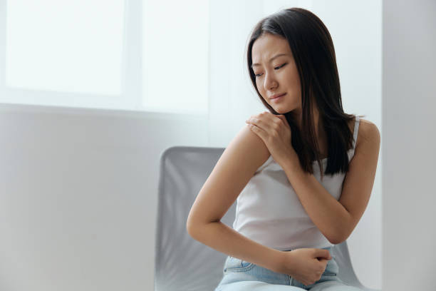 istock Suffering from neuralgia after sleeping in the wrong position tanned beautiful young Asian woman touching painful shoulder at home living room. Injuries Poor health Illness concept. Cool offer Banner 2147709561