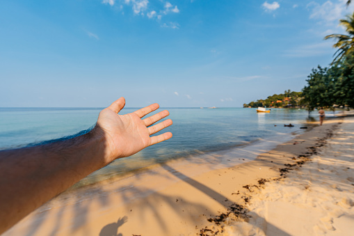 Young man's hand as he is showing the beautiful Ko Phangan beach on the Andaman sea in Thailand. His POV.