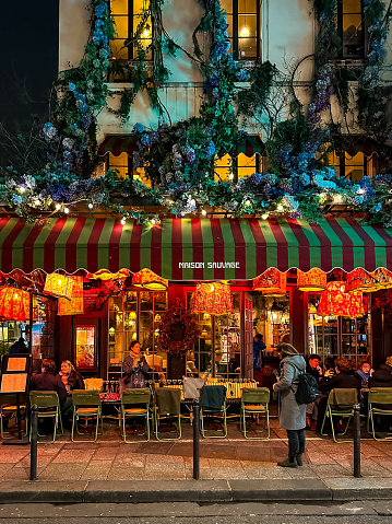 Paris, France - 20.02.2024. Maison Sauvage Saint-Germain-des-Prés french restaurant in Paris. Located at the cross of Rue de Buci and Rue Grégoire de Tours. illuminated at evening. incidental people are walking along the street
