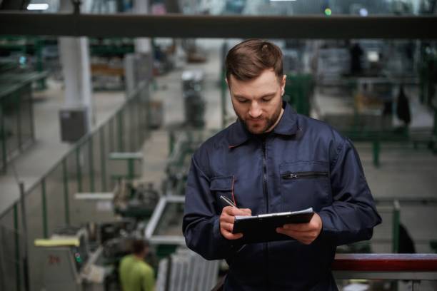 istock Writing information into the notepad. Factory worker is indoors with hard hat 2147711737