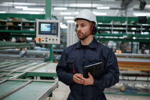 istock Machine behind, holding notepad. Factory worker is indoors with hard hat 2147711883