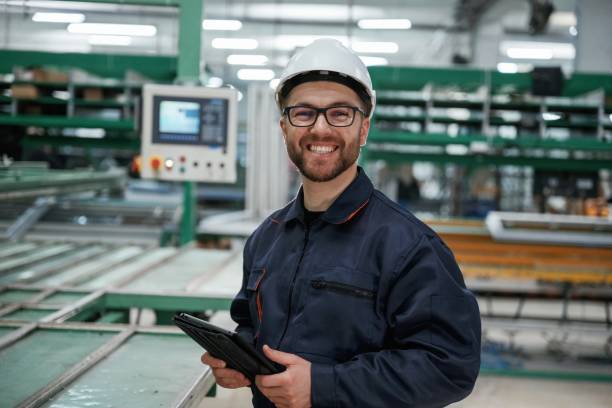istock Machine behind, holding notepad. Factory worker is indoors with hard hat 2147711948