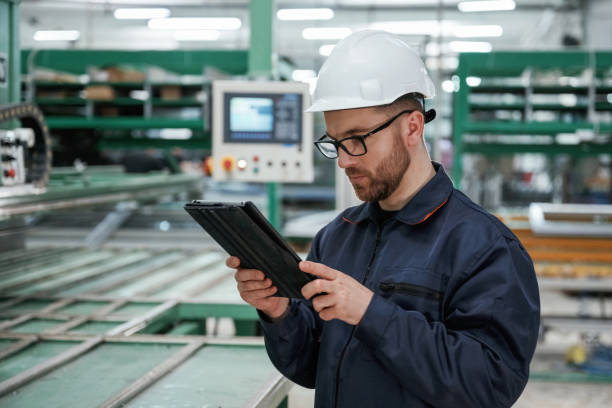 istock Machine behind, holding notepad. Factory worker is indoors with hard hat 2147711949