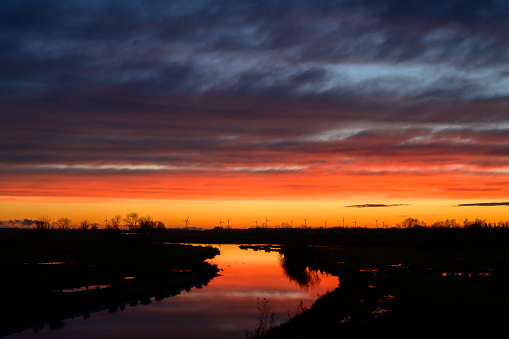 Panoramic view on the Reevediep Bypass waterway during a springtime sunset in Overijssel. The flow of the river is leading towards the setting sun in the distance at the end of a beautiful springtime day.
