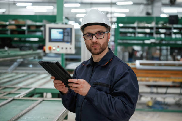 istock Machine behind, holding notepad. Factory worker is indoors with hard hat 2147711953