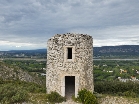 Photo of the stone Chappe telegraph tower in Orgon in the Alpilles with a magnificent landscape behind with the valley of the Durance under a cloudy sky. This photo was taken in Provence in France.