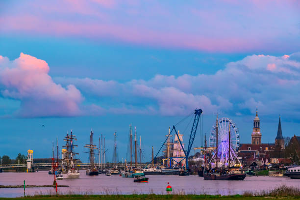 Kampen and river IJssel during the traditional fleet review or naval review at the start of the 2024 Sail Kampen event in the Hanseatic League city at the end of a springtime day with a colorful sunset in the sky.