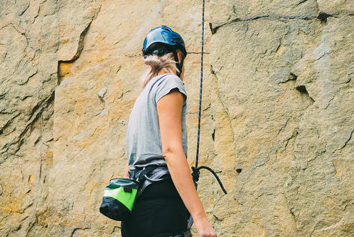 Young athletic woman in equipment standing in front of stone rock outdoors and getting ready to climb. Training area for outdoor activities. Extreme sport. Rear view