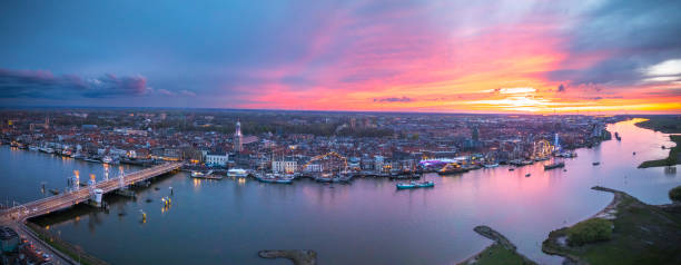 Kampen and river IJssel during the traditional fleet review or naval review at the start of the 2024 Sail Kampen event in the Hanseatic League city at the end of a springtime day with a colorful sunset in the sky.