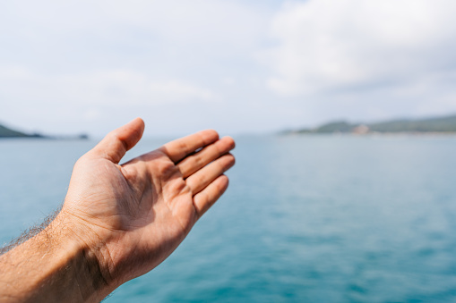 Young man's hand as he is showing Ko Phangan from the ferry in Thailand.