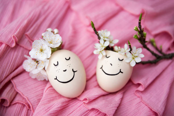 Easter painted Egg face with cherry blossom flowers decoration on pink cloth. Close up