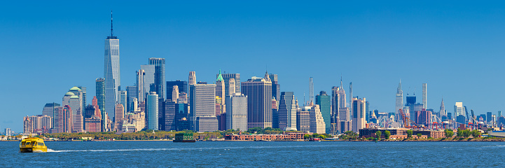 New York City Skyline with Battery Park, World Trade Center, Empire State Building, Chrysler Building, Manhattan Financial District, NYC Ferry Boat, Governors Island, Red Hook neighborhood of Brooklyn, Clear Blue Sky and Water of New York Harbor. High Resolution Stitched Panoramic image with 3:1 image aspect ratio. Canon EOS 6D Full Frame Sensor Camera and Canon EF 70-200mm f/4L IS USM Lens.
