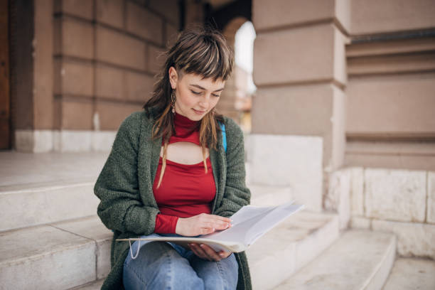 istock Young woman engrossed in her notebook, studying on urban steps 2147717415