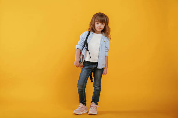 istock With backpack. Cute little girl is against yellow background 2147717573