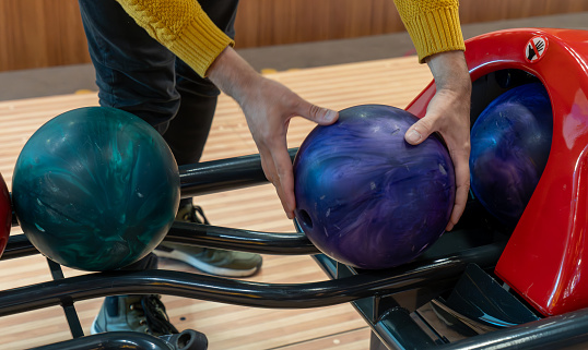 Person selecting colorful bowling balls from the rack at a bowling alley.