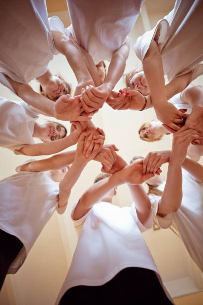 Group of teenage girls and boy wearing white t-shirts standing in circle in gym, holding hands and smiling at camera.
