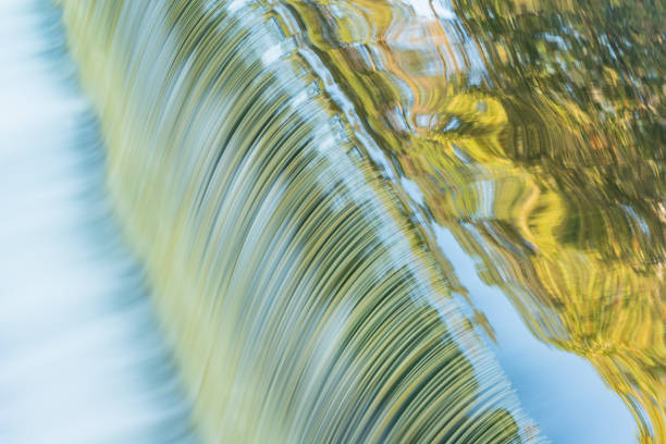 Battle Creek River cascade captured with motion blur and with reflections of autumn trees and sky in calm water, Michigan, USA
