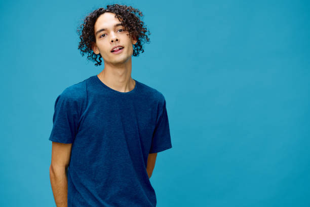 istock Smiling joyful cute curly tanned Caucasian guy in basic t-shirt posing isolated on over blue background. Lifestyle and Emotions concept. Good offer with copy space for ad 2147724503