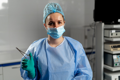female surgeon in a mask in the operating room stands with a sterilized clamp