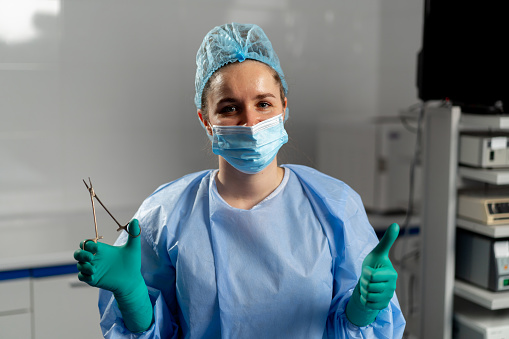 female surgeon in a mask in the operating room stands with a sterilized clamp and shows a super finger