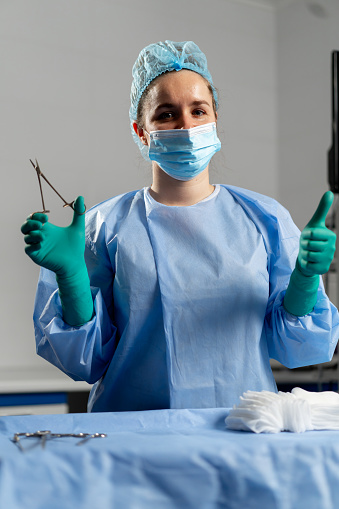 female surgeon in a mask in the operating room stands with a sterilized clamp and shows a super finger