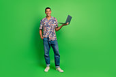 Full length portrait of positive young man hold use apple microsoft laptop empty space isolated on green color background